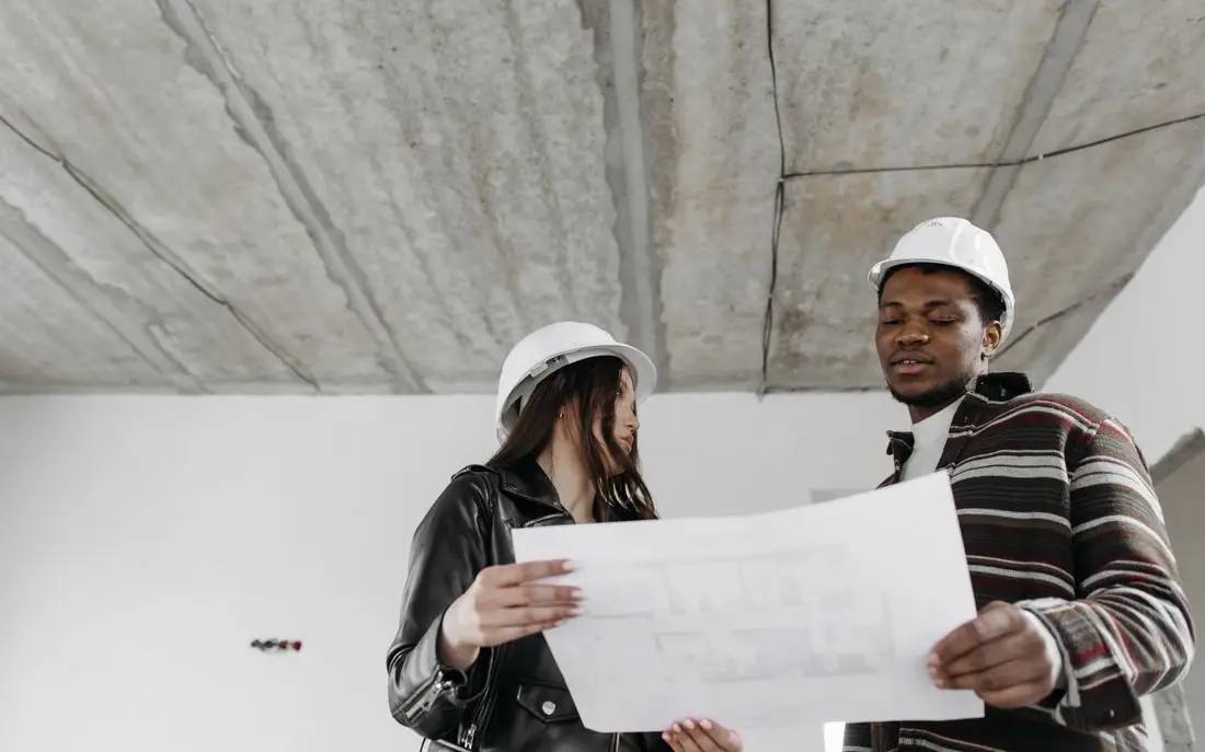 Two site managers in hard hats checking drawings in a building under construction